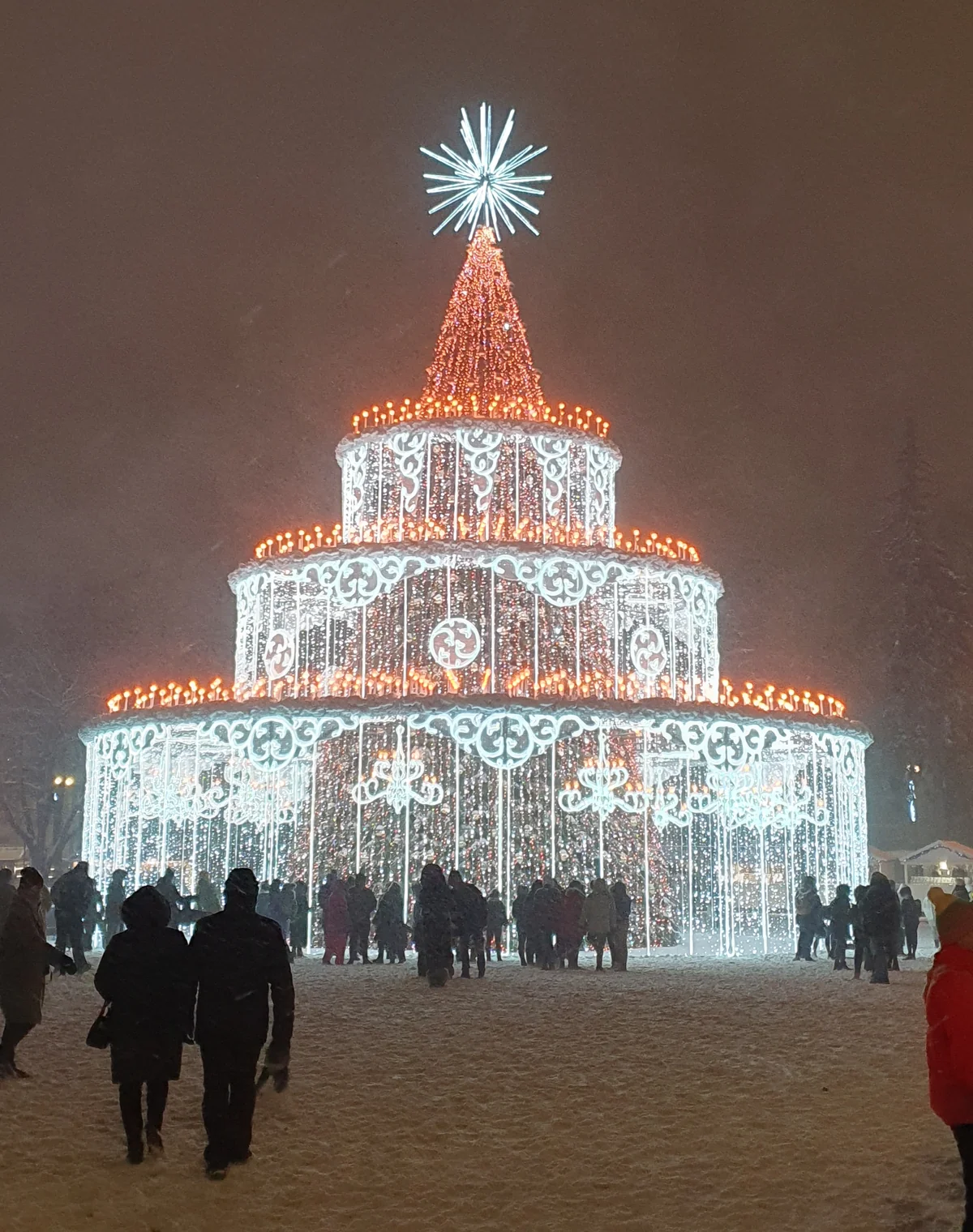 Kalėdų eglė Vilniaus Katedros aikštėje 2022 m. žiemą, apšviesta baltomis ir oranžinėmis švieselėmis.